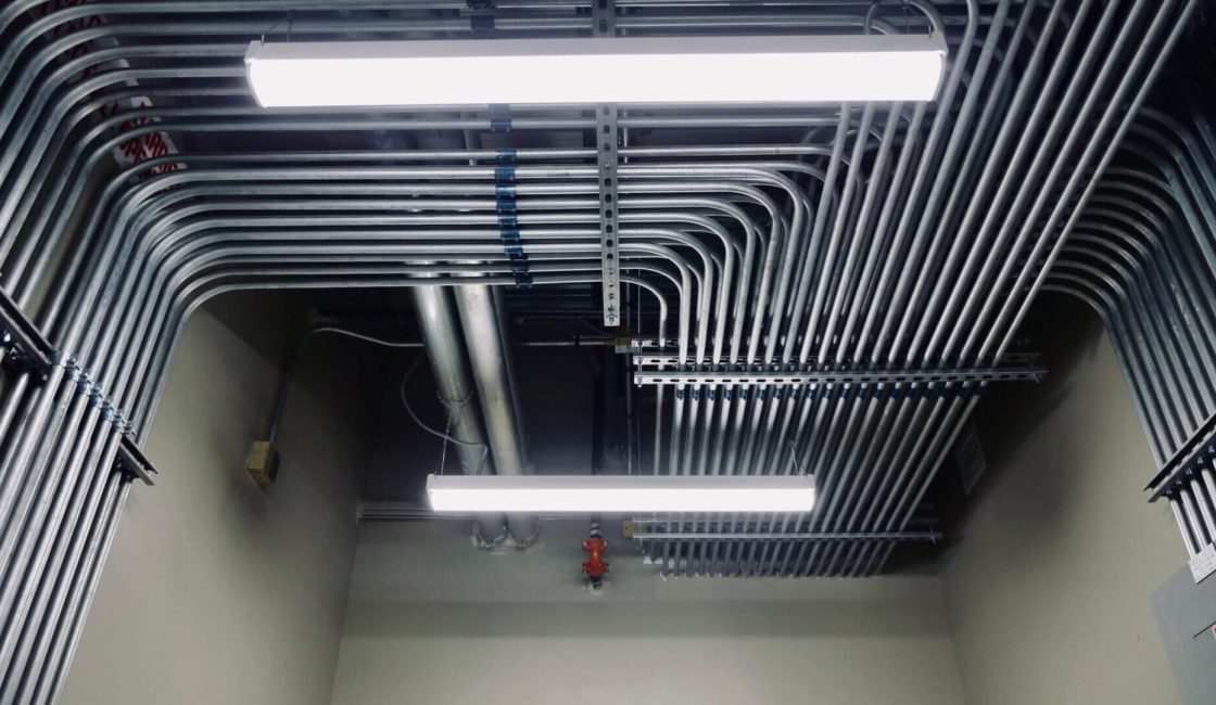 A ceiling with many pipes and wires hanging from it.