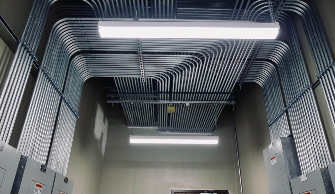 A ceiling with many pipes and wires hanging from it.