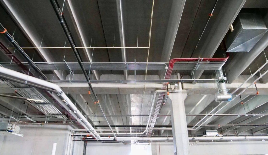 A ceiling with pipes and wires hanging from the ceiling.