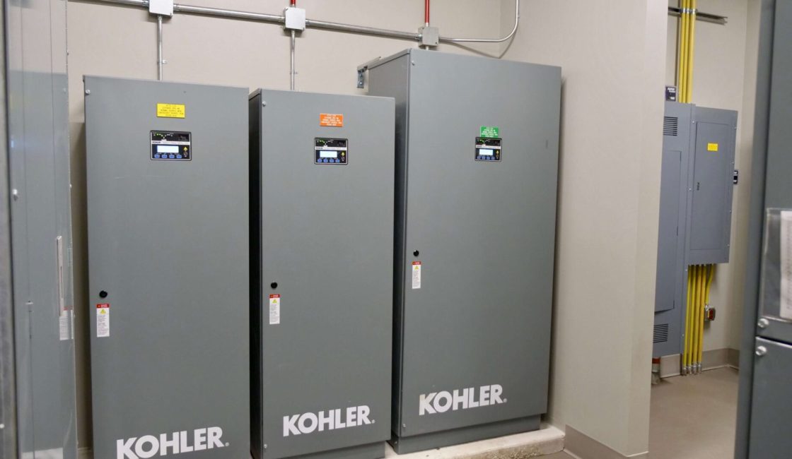 Three electrical cabinets in a room with wires plugged into them.